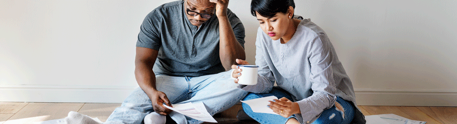 A man and a woman are looking at their bills spreading all over the floor.